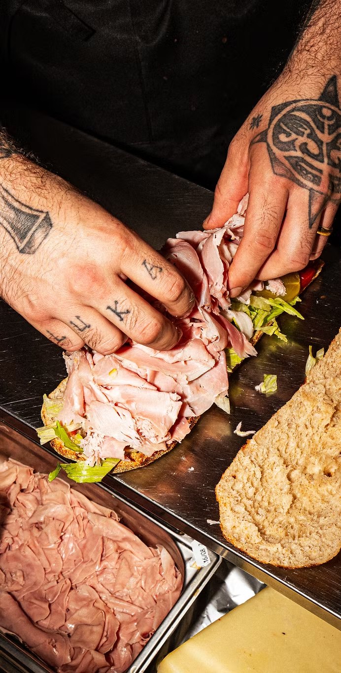850° Oberkampf – tattooed hands building a hero sandwich