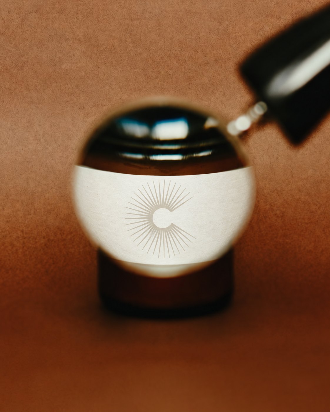 Optique Carnot – amber bottle with sun monogram label seen through a lens, packaging by Jon Filin